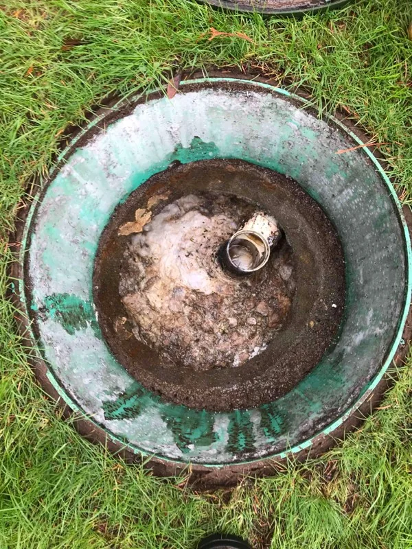 Looking down a green riser at a concrete lid, with a pipe stub standing proud of it.