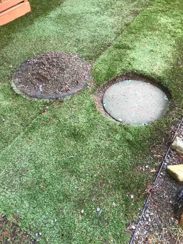 Two access points in the back lawn, one still covered over with soil and one dug clear to its concrete lid.