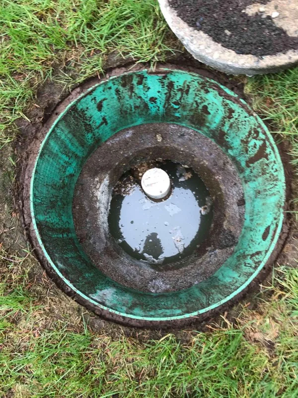 Looking down a green riser at the tank lid below, with a small inspection cap and standing water on top of it.