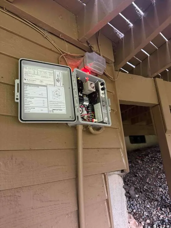 The control panel mounted on the house wall with its cover open and the alarm light lit.