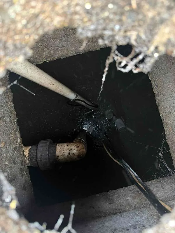 Looking down a square access opening at pipework and float cables over dark liquid.