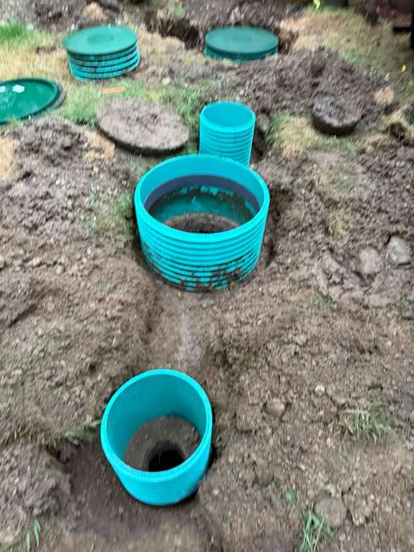 Two new riser sections set in the trench, the larger over the tank and the smaller alongside.