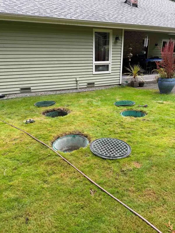 Five access lids in the back lawn, several lifted clear, with the house behind.