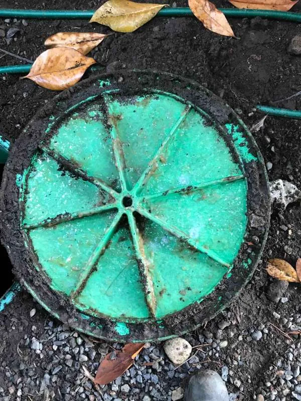 A segmented riser lid lifted off and set down on the ground beside its opening.