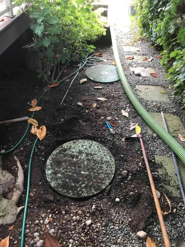 The side passage beside the house, with the suction hose run along it between two tank lids.